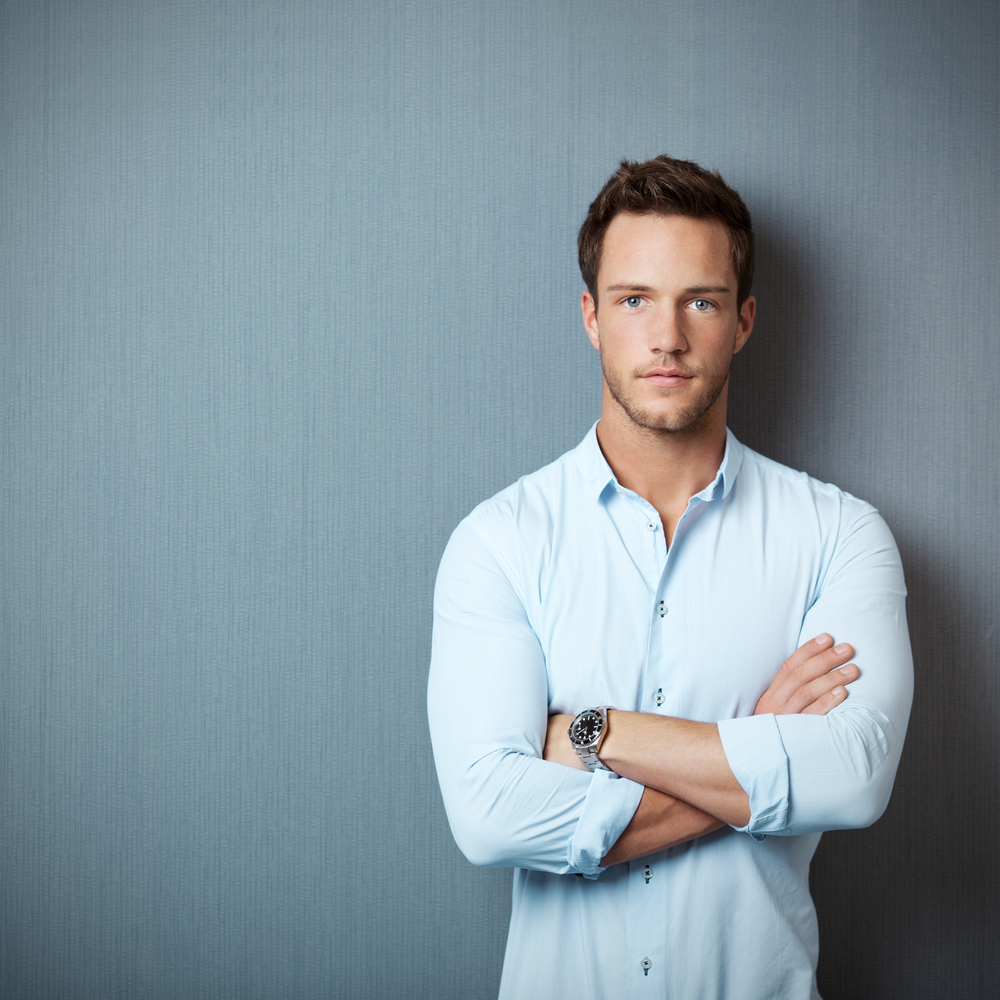 Portrait of a smart serious young man standing against blue background